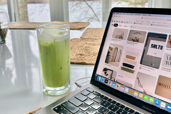 Laptop sitting on table open to Pinterest showing branding ideas, fonts, and color palettes, and a glass of a green drink sitting next to the laptop on the table.